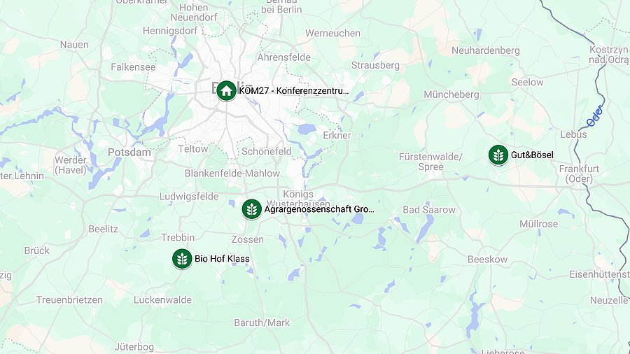 A map of Berlin and its surrounding areas, featuring four dark green location markers. The first marker is positioned in the center of Berlin, labeled 'KOM27 – Konferenzzentrum Mauerstrasse.' To the south of Berlin, three additional markers are placed from west to east: 'Biohof Klaas,' 'Agrargenossenschaft Groß Machnow eG,' and 'Gut und Bösel.'